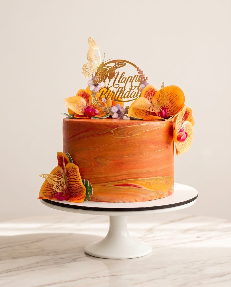 Gâteau d'anniversaire marbré orange, orchidées et papillon doré