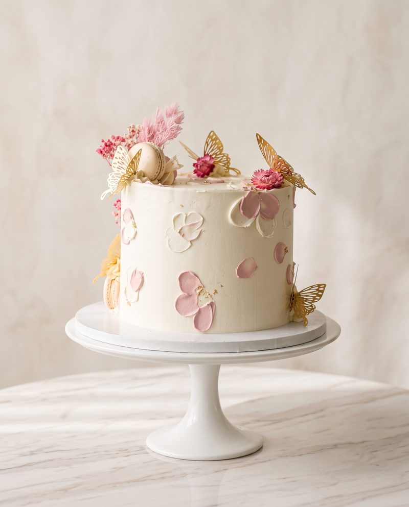 Gâteau d'anniversaire blanc, pétales roses, macarons et papillons dorés